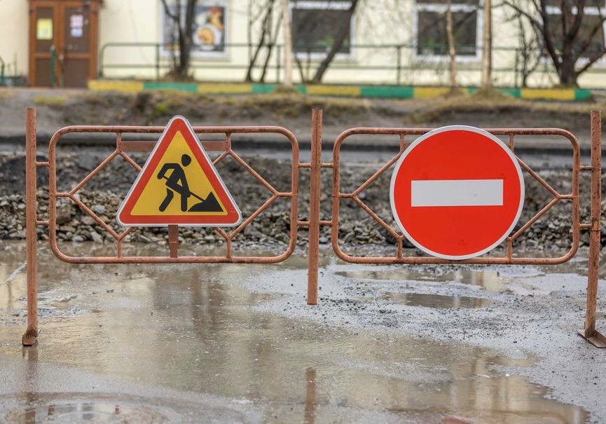Close-up of construction signs and barriers in a muddy area outdoors, indicating no entry