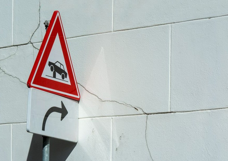 Traffic warning sign on a cracked white wall, indicating a turn ahead